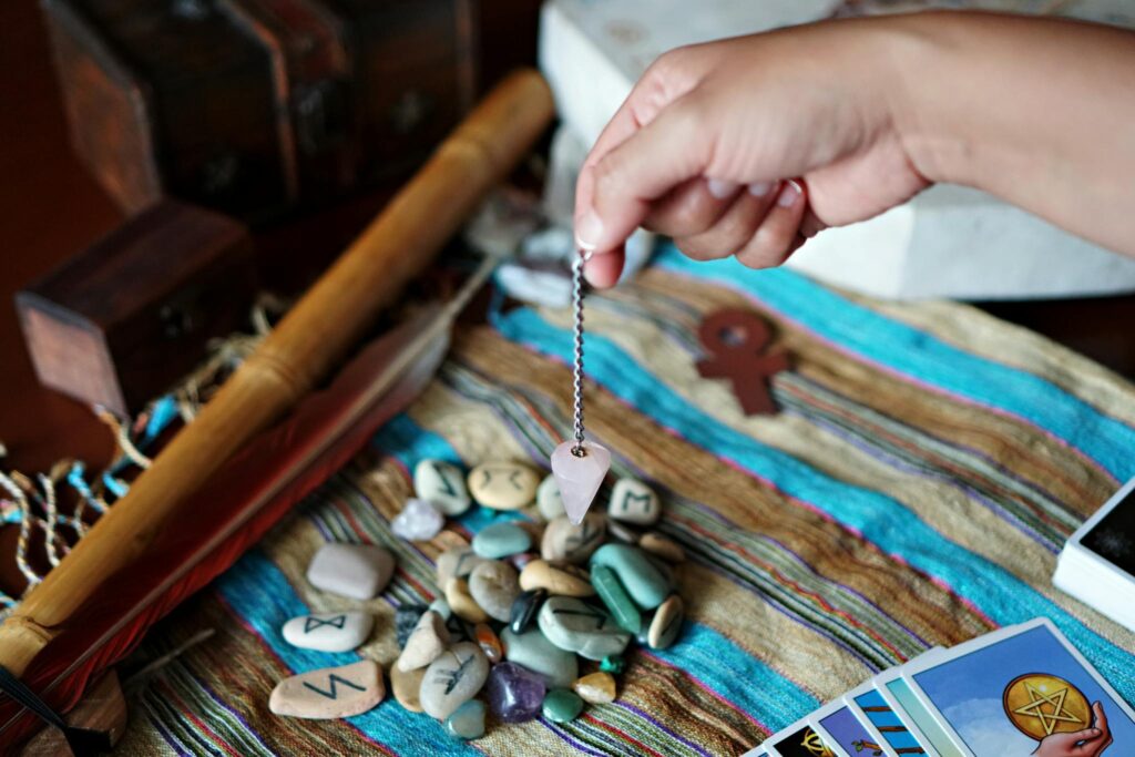A mystical scene featuring a hand using a pendulum over runes and tarot cards.
